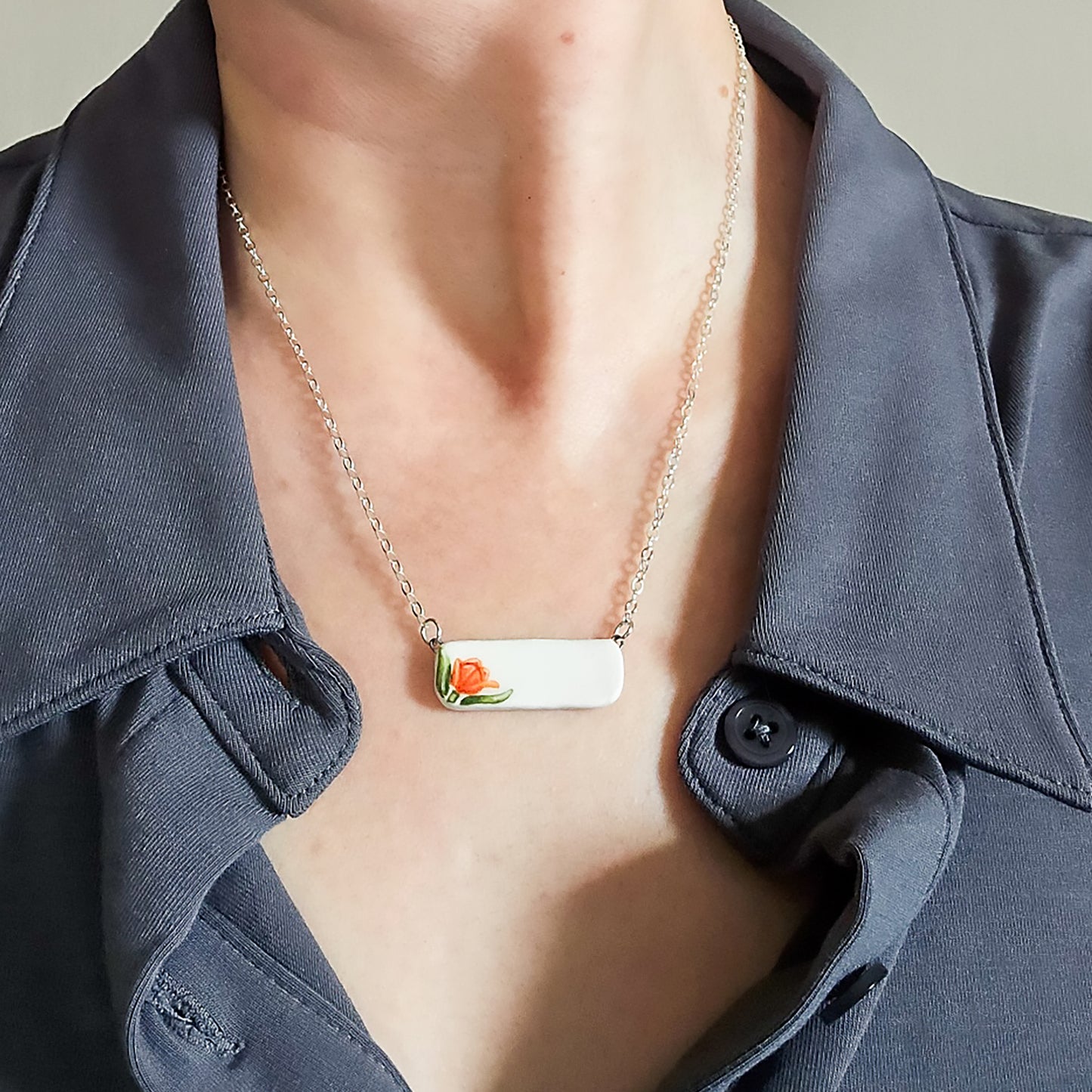 White bar pendant with orange tulip is worn by a model.