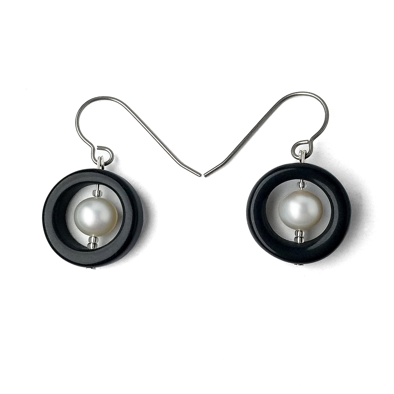 Porcelain and Pearls Earrings.  For each earring, a ring of rich black  porcelain frames a cultured freshwater pearl and is suspended from titanium hooks.  Earrings are displayed on a white background.