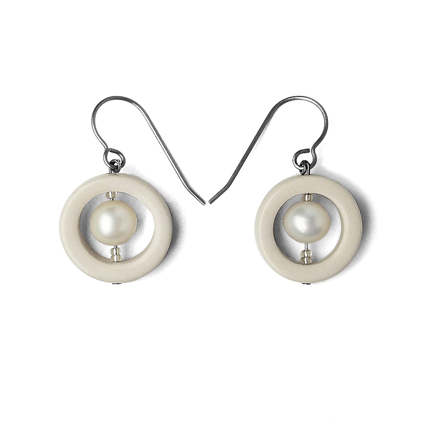 Porcelain and Pearls Earrings.  For each earring, a ring of creamy white porcelain frames a cultured freshwater pearl and is suspended from titanium hooks.  Earrings are displayed on a white background.